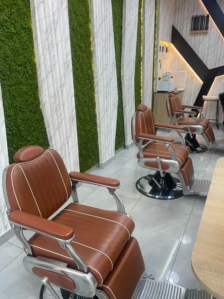 Tan leather barber chairs lined up against a living moss and marble wall